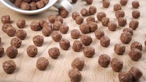 Chocolate cereal balls are scattered over the board with a white teacup. Round flakes. Close-up. Dolly Shot