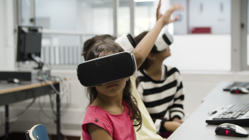 Multietnic children wearing virtual reality glasses. Concentrated kids sitting in classroom, using modern technology. Excited boy and girl rising their hands up. VR technology in education concept. | Shutterstock HD Video #1072280270
