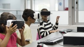 Multiethnic children wearing VR headset and sitting at desk. Dark-haired girl imagining that she plucking something and cutting it off. Boy raising his hands up. VR technology in education concept. - Powered by Shutterstock - Get 15% off with code: PIKWIZARD15