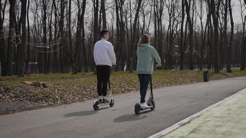 A beautiful couple of young people ride in the park on electric scooters