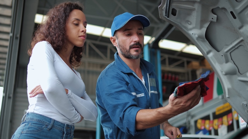 Mechanic man checking engine oil level to woman customer and discussing repairs done to her vehicle at the repair garage. Royalty-Free Stock Footage #1072281299