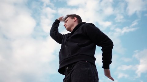 Man Street Dancer Moves in a Dance. Guy Moves in the Style of Martial Arts against the background of a Beautiful Sky. Bottom View. Camera Rotates 360 Degrees. Slow Motion.
