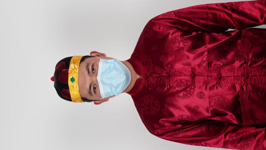 Portrait of 
Chinese young man in beautiful costume dress wearing a protective face mask on white background. Dust protection against virus. Coronavirus pandemic and infection.