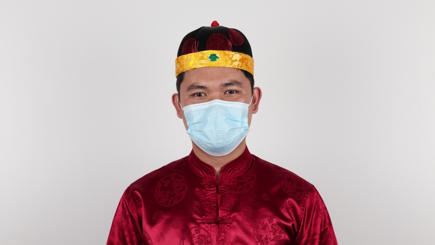 Portrait of 
Chinese young man in beautiful costume dress wearing a protective face mask and salute etiquette palm and fist gesture bounding .on white background. 