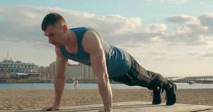 Daily physical exercise to be in good shape. Adult attractive muscular 30 year old man doing push-ups on the city beach.