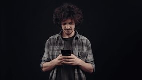 The charismatic young man, in love, writes a message, puts his hand thoughtfully behind his head and then continues to text. Isolated on black background, Concept of life. People's emotions. 4k - Powered by Shutterstock - Get 15% off with code: PIKWIZARD15