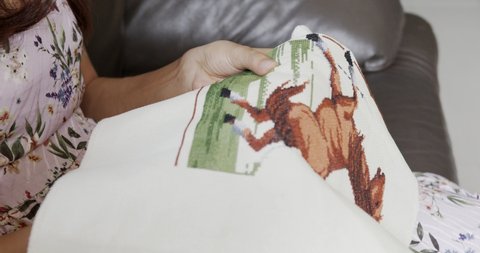 Woman hands doing cross-stitch of picture of a skittish horse at home, close up of embroidery. 