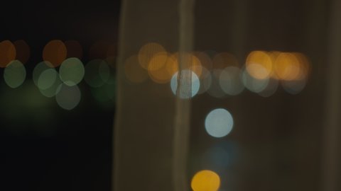 Blurred background from a night window covered with tulle. City lights