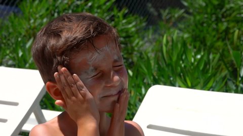 Tanned boy is smearing himself with a sun protection cream on the sunny day