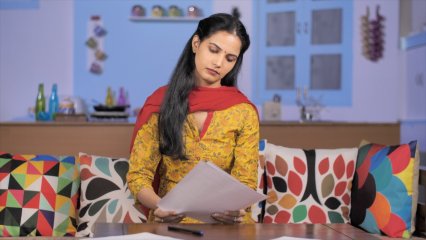 Young Indian homemaker puts a signature on an official paper - Insurance documentation . Medium shot of an attractive businesswoman finishing her paperwork signing contract sitting at home