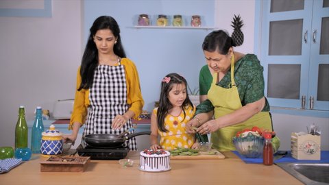 Little urban girl learning kitchen work from her mother and grandmother at home - Family bonding. Three generations of ladies having a fun time while cooking together - healthy relationship and lif...