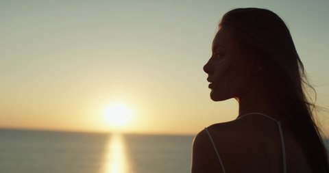 Close up portrait of beautiful woman enjoying peaceful sea horizon sunset. Wind blowing on hair. 4K shot.