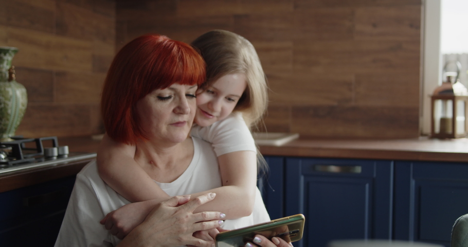 Grandmother and child using a smartphone together. Grandparent and grandchild looking at phone screen touching it. Aged woman and little girl playing a game on a cellular phone.