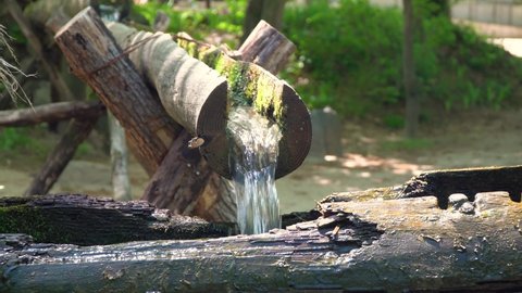 Water from wooden pipe Slowly Fills A Hollow On Wood On A Traditional Korean Mill Then Suddenly Tips In Korean Folk Village, Yongin, South Korea. - close up