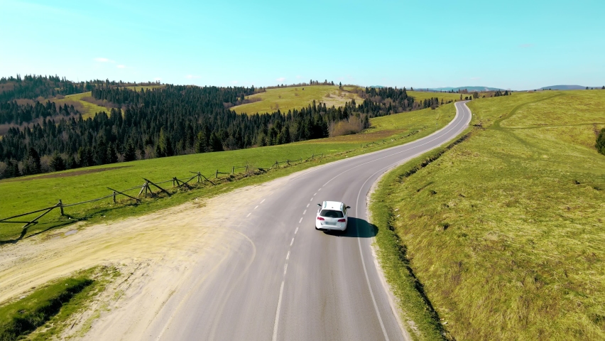 Aerial view white car travels in beautiful mountainous terrain. One car driving on an asphalt road with a beautiful landscape. Royalty-Free Stock Footage #1072316771