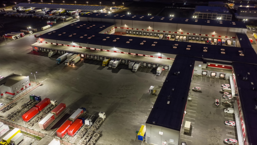 Aerial hyper lapse (motion time lapse) of a logistics park with a loading hub. Semi-trailers trucks stand at warehouse ramps for load and unload goods at night. | Shutterstock HD Video #1072321457