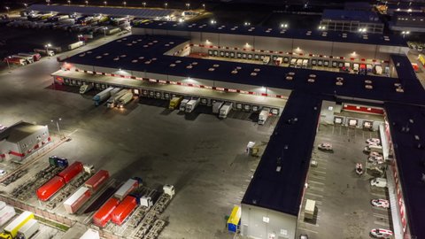 Aerial hyper lapse (motion time lapse) of a logistics park with a loading hub. Semi-trailers trucks stand at warehouse ramps for load and unload goods at night.