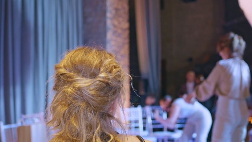 A girl with blond hair, a beautiful evening hairstyle and evening dress is resting in a cozy place, enjoying a drink. Other vacationers are taking photographs of the girl with flowers. Royalty-Free Stock Footage #1072333223
