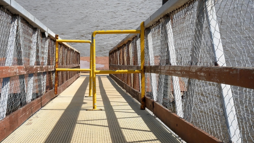 Metal handrails on dock ramp slope leading to calm rippling lake water dolly left