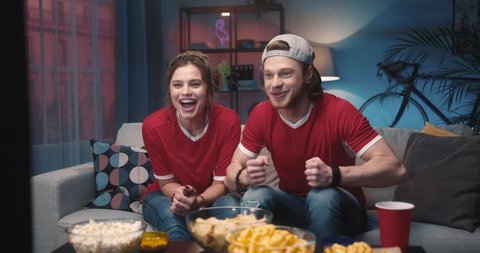 Caucasian joyful happy young couple woman and man at home hanging together cheering for favorite team and it winning match. Friends watching game on TV on sport channel, fun concept