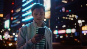 Portrait of Man Using Smartphone Walking Through Night City Street Full of Neon Light. Smiling Stylish Man Using Mobile Phone, Social Media, Online Shopping, Texting on Dating App. Medium Shot - Powered by Shutterstock - Get 15% off with code: PIKWIZARD15