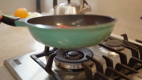 The cook holds a frying pan over the gas stove. Cooking healthy food.