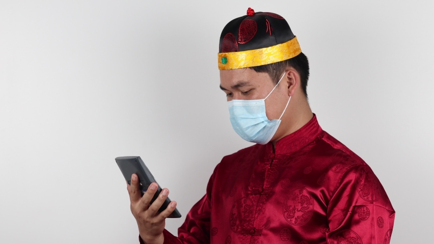 Portrait of young Asian man Chinese in beautiful costume dress pressing a calculator on white background. 