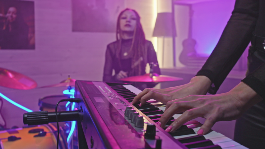 Slow-motion midsection closeup of unrecognizable female hands playing electronic keyboard synth during rock concert while female drummer with dreadlocks playing drums in background Royalty-Free Stock Footage #1072354064
