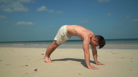With butt in the air, man does pike pushups on a tropical beach.