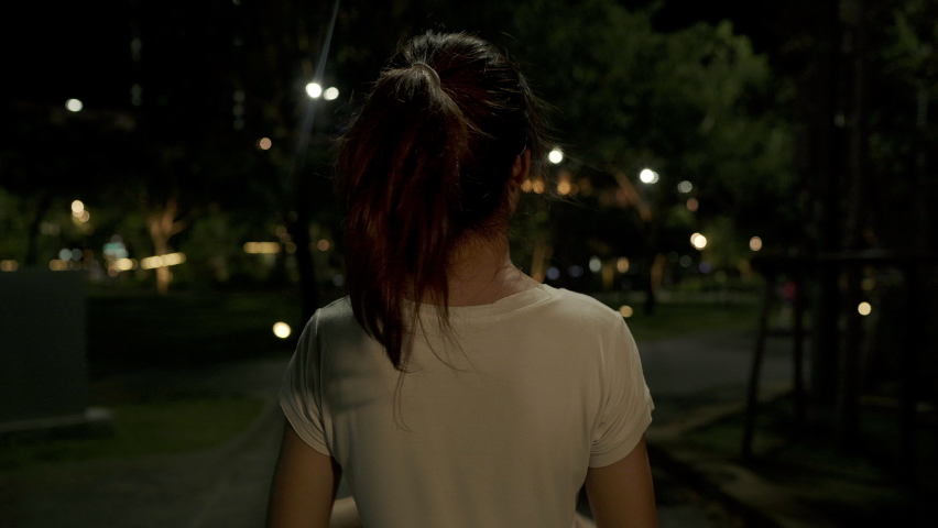 Young happy asia girl relax walk on footpath and cheerful smile looking at camera around tree in park at city night. Beautiful nature in the city view, Travel holiday vacation activity concept.