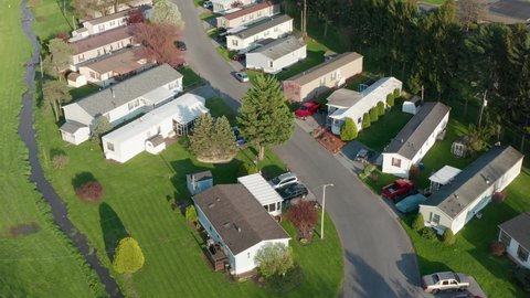 Aerial tilt up reveals many mobile homes. Trailer park with street during spring scene in USA.