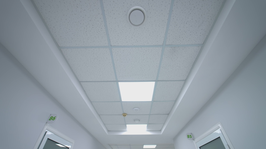 Long corridor with lamps in the hospital. Details of ceiling with lights and framing. Perspective view from a moving stretcher. Motion camera back. Royalty-Free Stock Footage #1072375349