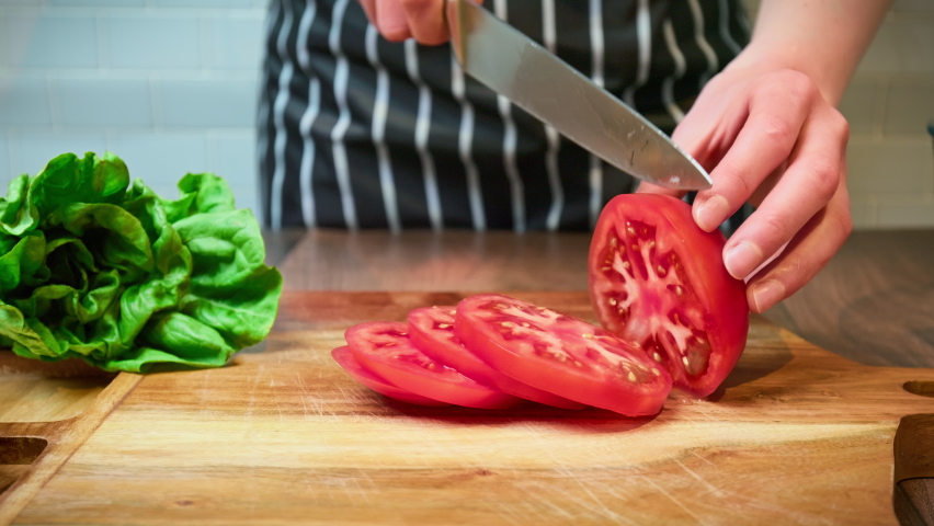Close-up of chopping red tomatoes on a wooden cutting board in 4K. Preparing food ingredients in slow motion.