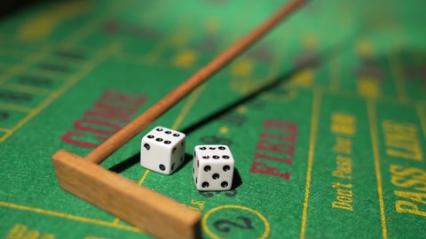 This close up, POV video shows a craps dealer using a rake to pulls back a pair of rolled dice on a green felt craps table.