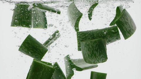 Slow motion shot of aloe vera cuts falling into water on white background
