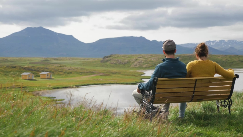 Female and male Couple sitting on wood bench at the Snaefellsnes Peninsula Iceland with panoramic view, Locked back shot