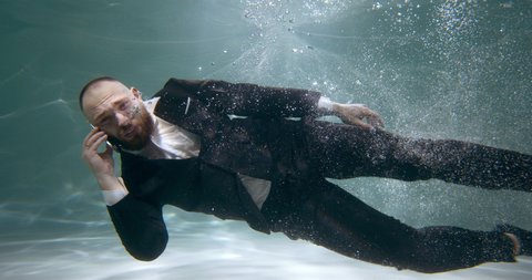 Amazing cinematic view of young stressed angry boss businessman swimming underwater talking on the phone slow motion.