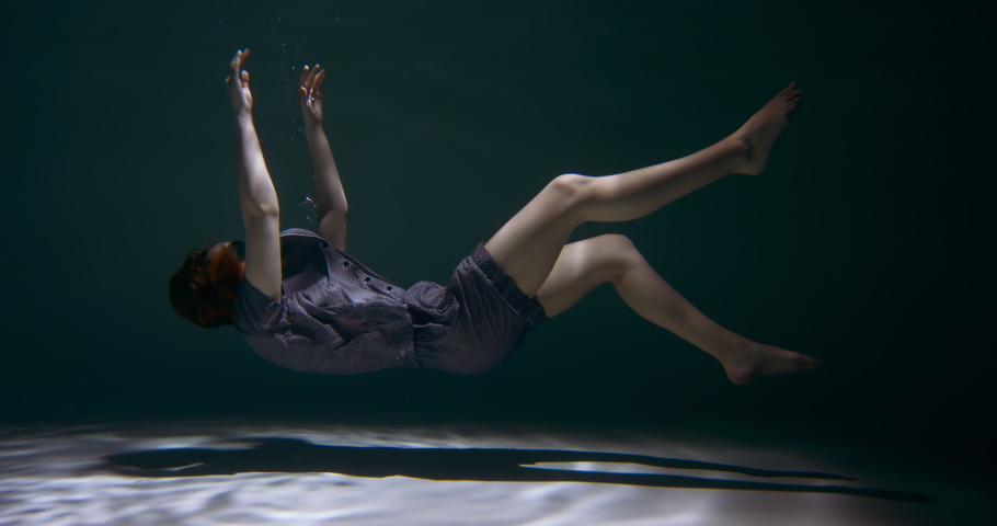 FALLING ASLEEP. Incredible view of young beautiful woman in pyjamas, sleep mask sinking under water dreaming slow motion