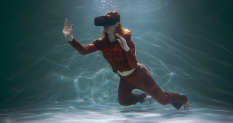 Concept of virtual reality. Beautiful young happy red haired woman using VR headset floating under water slow motion.