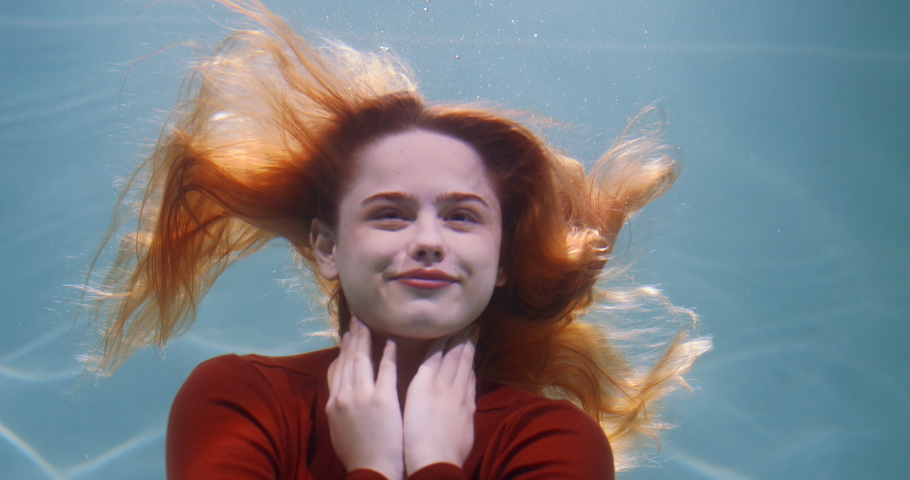 Natural beauty concept. Cinematic portrait of young beautiful redhead woman spreading hair deep under water slow motion.