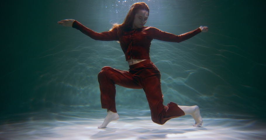 Happiness concept. Cinematic shot of young beautiful happy redhead woman doing fun dance moves under water slow motion.