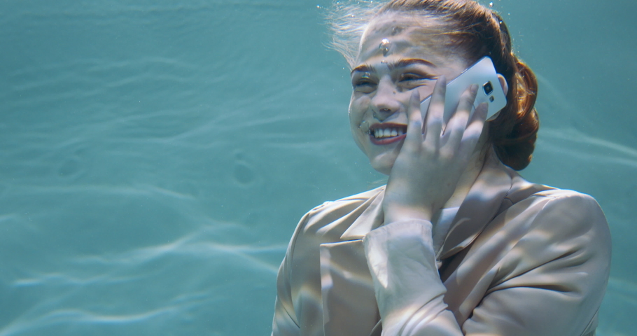Amazing under water portrait of happy beautiful young redhead business woman in office suit talking on phone slow motion
