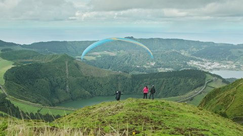 Miradouro da Vista do Rei, Sao Miguel, Azores, Portugal 2021. Aerial view of unique landscape surrounded with volcanic craters. A paragliding pilot takes off as seen from a hill. High quality footage