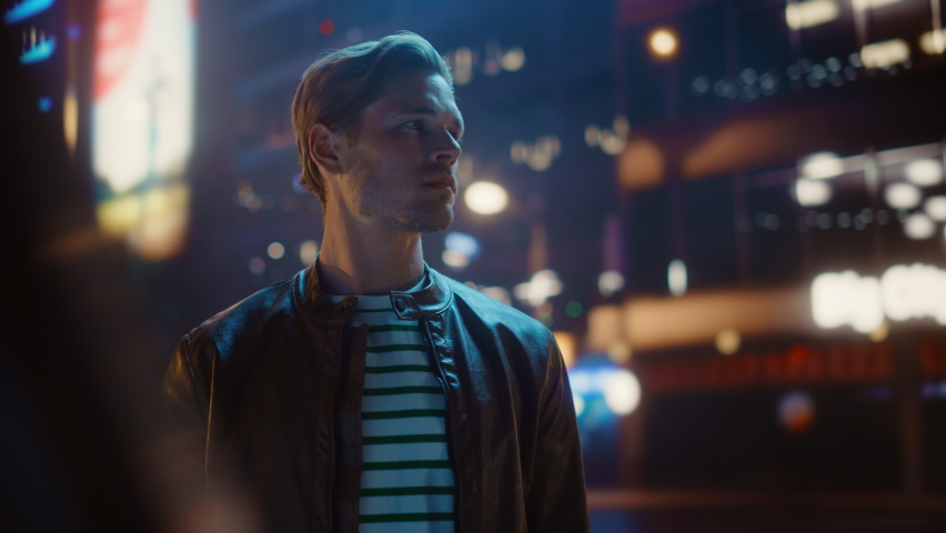 Portrait of Handsome Serious Man Standing, Looking Around Night City with Bokeh Neon Street Lights in Background. Focused Confident Young Man Thinking Tracking Dolly Arc Medium Shot with Flares | Shutterstock HD Video #1072389953
