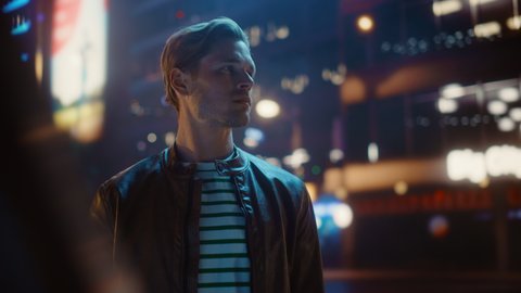 Portrait of Handsome Serious Man Standing, Looking Around Night City with Bokeh Neon Street Lights in Background. Focused Confident Young Man Thinking Tracking Dolly Arc Medium Shot with Flares