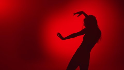 Silhouette of sexy woman dancer performing dance movement waving hair enjoying freedom slow motion. Shadow of seductive female raising hands dancing in red darkness. 4k Dragon RED camera
