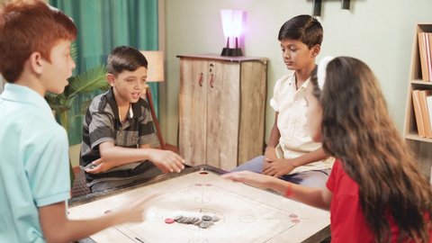 Group of kids fighting to decide for pair to play carrom by clapping or flipping hands on carrom board at home - Concept of childhood holiday lifestyle and summer vacation.