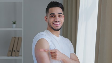 Portrait of arabic ethnic hispanic man guy patient shows medical plaster on shoulder demonstrates injection mark happy satisfied after vaccination with covid-19 virus vaccine smiling looks at camera
