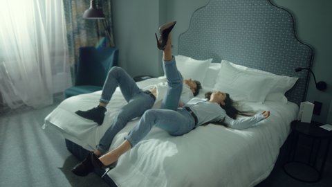 Top view attractive couple jumping backwards on hotel bed. Cute couple resting in luxury hotel suite. Romantic man and woman enjoying vacation in modern interior bedroom. Love couple at hotel