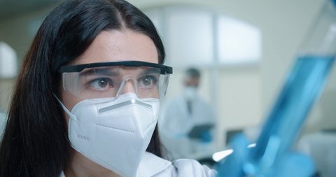 Close up of Caucasian beautiful woman chemistry researcher in laboratory working testing microbiology blue liquid Young female medical scientist working on coronavirus cure looking at test tube in lab